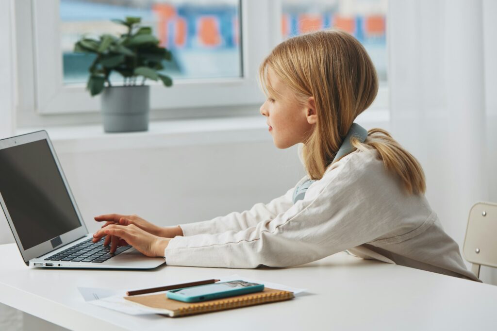 Smiling teenage girl learning at home using laptop for elearning She sits at a modern desk with