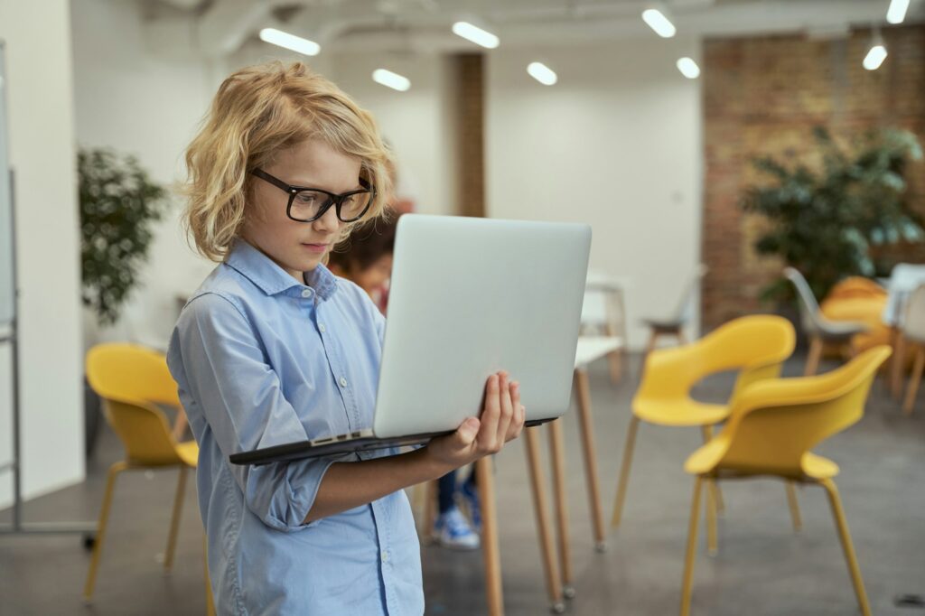 The future of IT. Portrait of little genius boy in glasses holding and using laptop while posing in