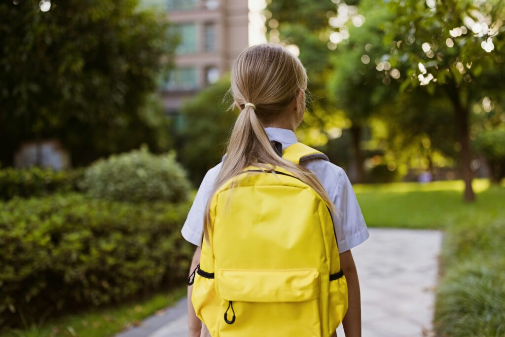 Back to school. Little girl with yellow backpack from elementary school outdoor. Kid going learn new