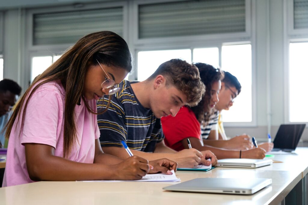 African american teen high school student writing in class. College students taking notes in class.