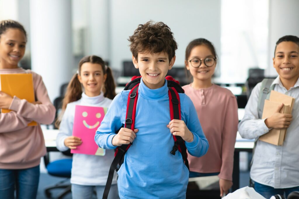 Smiling international schoolchildren standing and posing at classroom